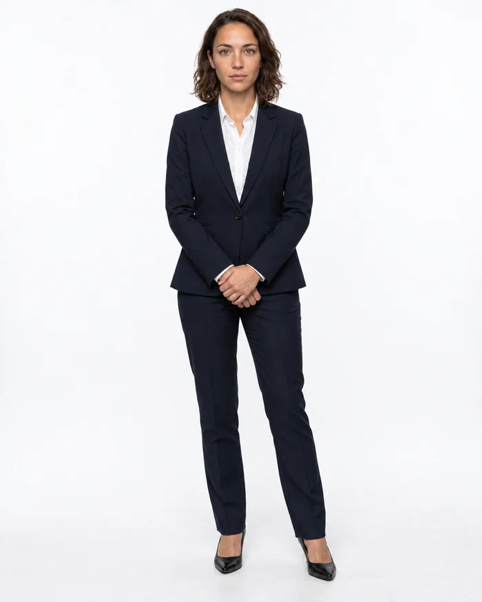 Full-length studio photograph of an AI-generated female model in a navy suit and white shirt, standing against a white background.